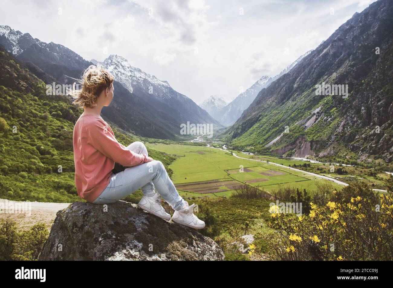 Une belle jeune fille est assise sur un rocher dans les montagnes et regarde le beau paysage d'une vallée de montagne avec de beaux nuages Banque D'Images