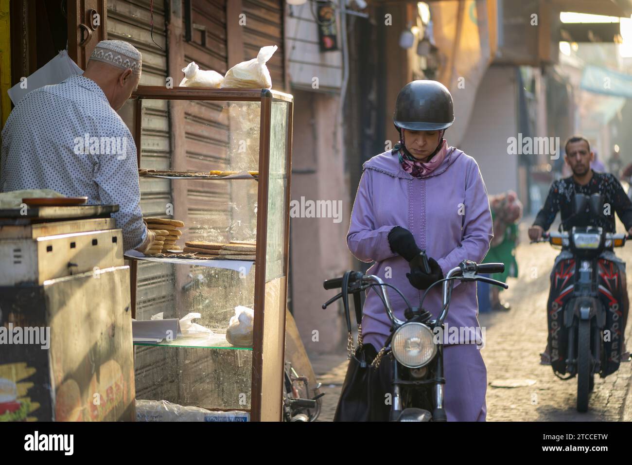 Marrakech, Maroc : une femme marocaine sur un scooter achète du pain frais dans une boulangerie à l'intérieur de la Médina de Marrakech. Banque D'Images