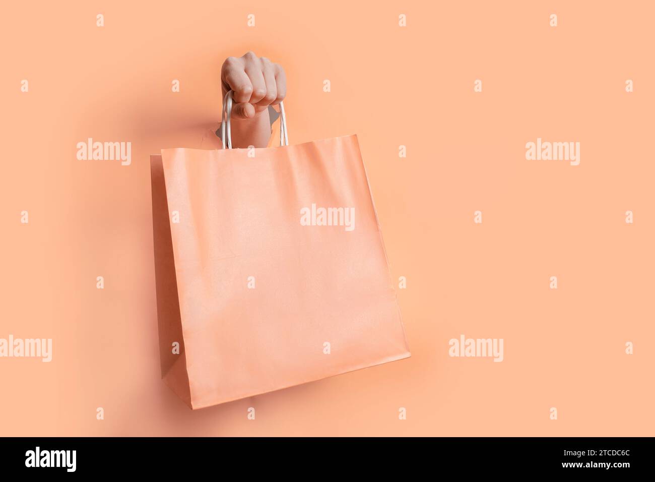 Main féminine tenant le sac en papier couleur fuzz pêche à travers le trou en toile de fond de papier Banque D'Images
