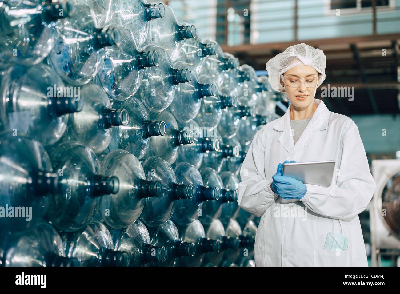 Les travailleuses travaillant dans l'usine d'eau potable inspectent le comptage des stocks de bouteilles de contrôle d'entrepôt de comptage avec l'uniforme d'hygiène. Banque D'Images