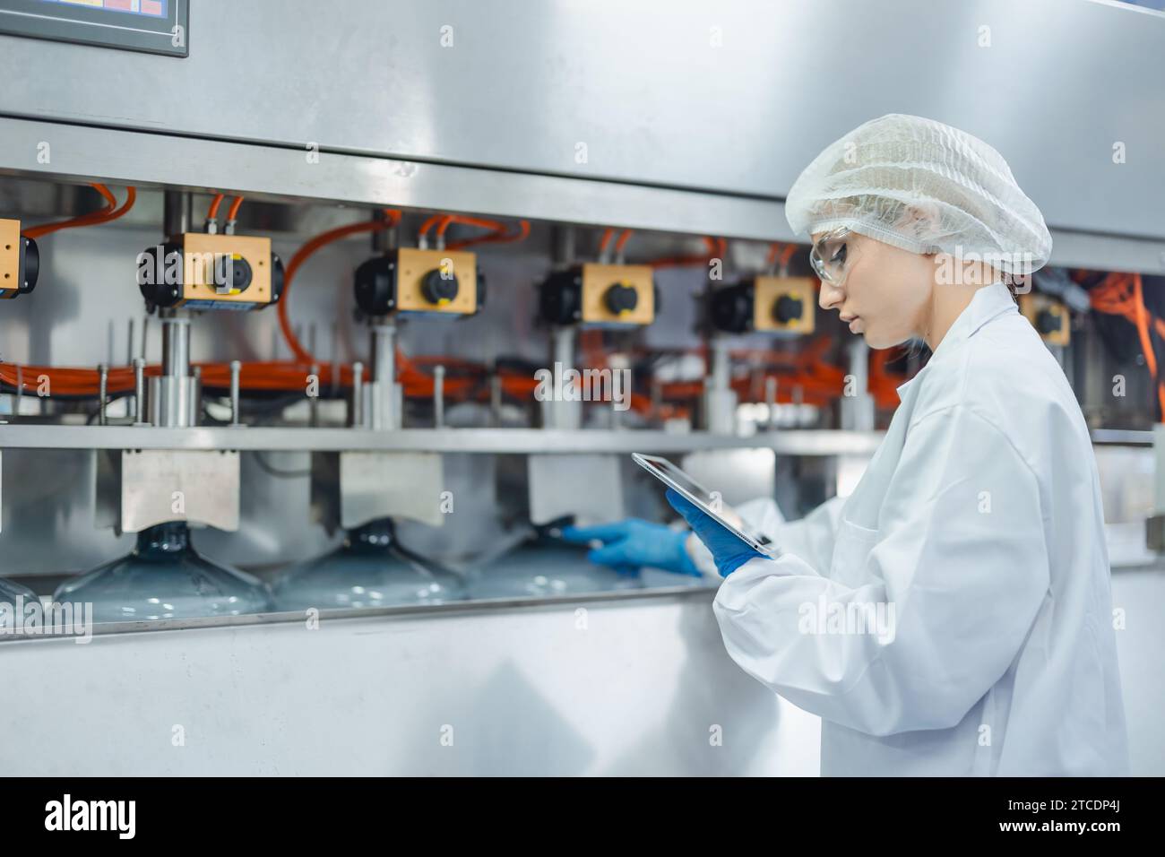 les femmes caucasiennes travaillant dans le processus d'hygiène propre d'usine d'usine d'eau dans la ligne de machine d'embouteillage d'eau potable. Banque D'Images