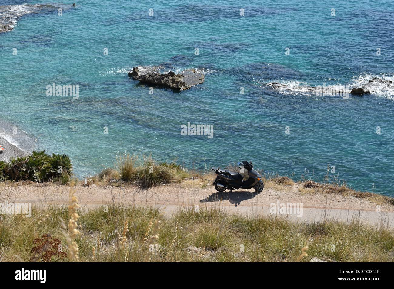 Un scooter Vespa debout sur le bord d'une petite route le long de la mer en Sicile Banque D'Images