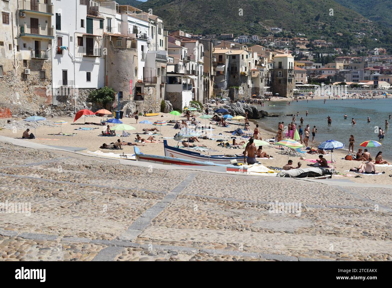 Bâtiments en bord de mer en face de la plage peuplés de personnes profitant de la journée et nageant à la plage de Cefalù Banque D'Images