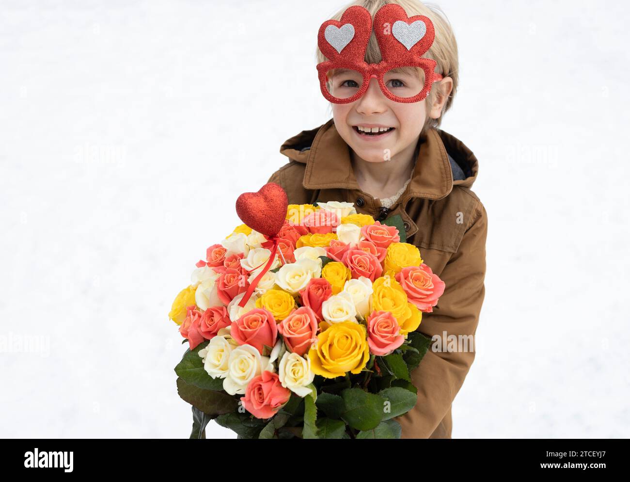 mignon garçon 6 - 7 ans tient un grand bouquet de roses sur un fond enneigé clair. Fête des mères. Journée internationale de la femme. Portrait d'un enfant heureux Banque D'Images