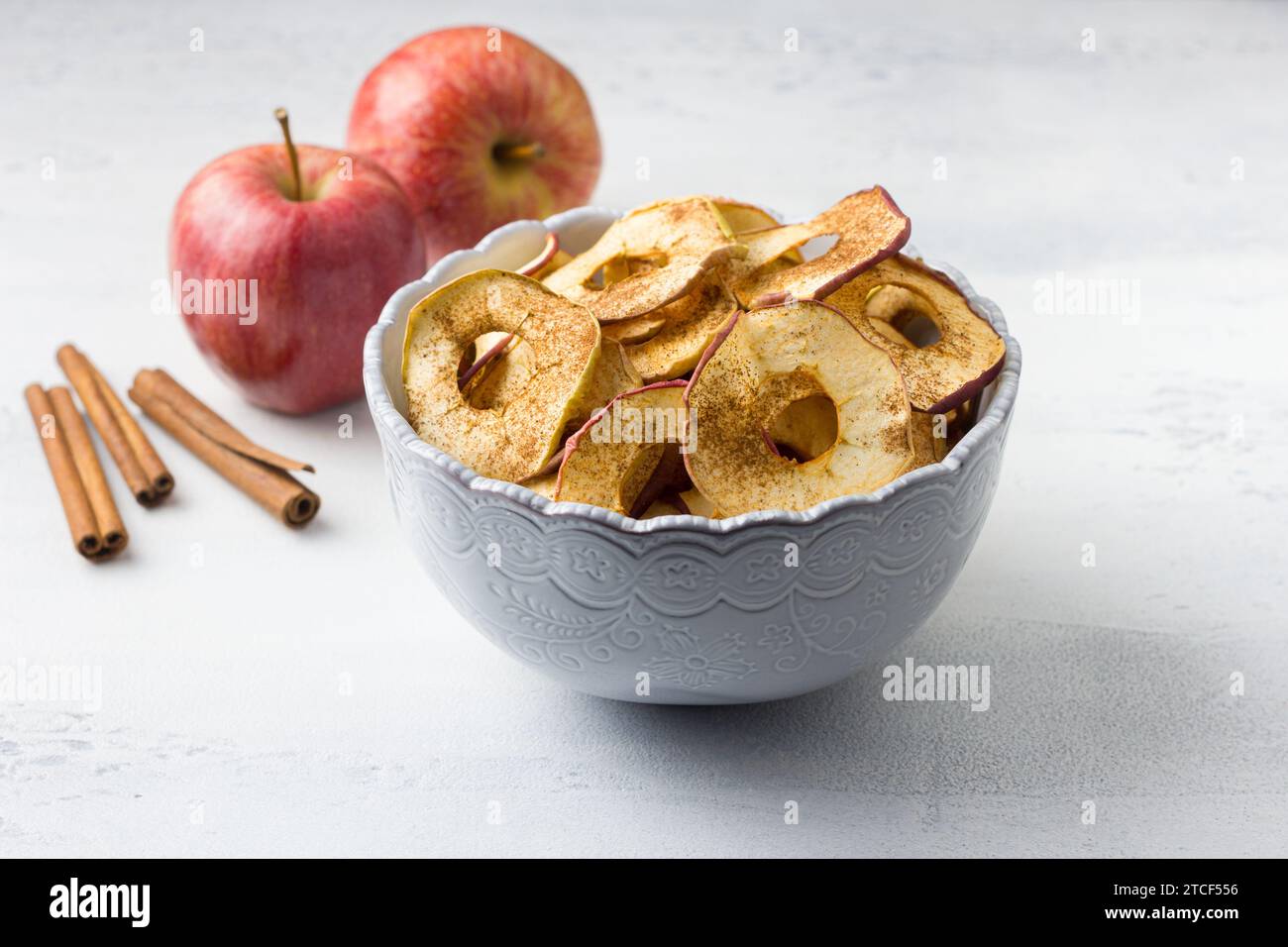 Pommes séchées maison à la cannelle, chips de pomme dans un bol avec des bâtons de cannelle sur un fond gris clair. Délicieux en-cas sain Banque D'Images