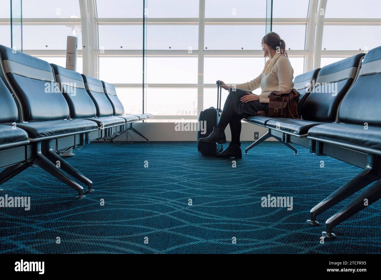 femme assise regardant par le verre d'un terminal d'aéroport Banque D'Images