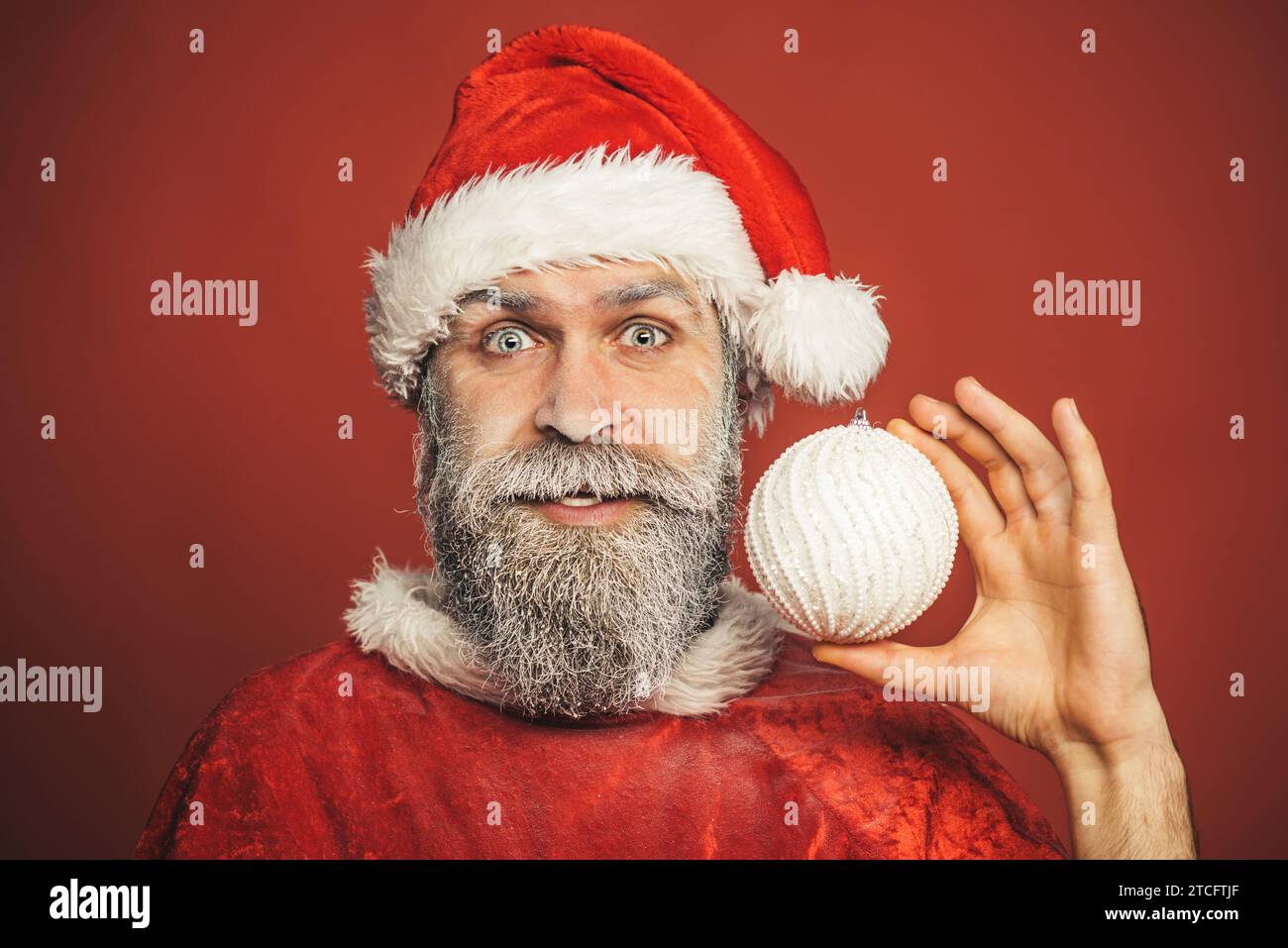Père Noël drôle avec boule de Noël blanche. Décorations et ornements de vacances. Noël et fête du nouvel an. Homme barbu en vêtements de Père Noël Banque D'Images