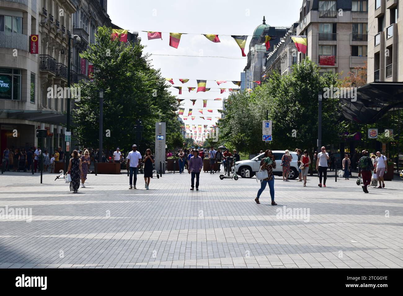 Des gens marchant sur le boulevard Anspach dans le centre-ville de Bruxelles par une journée ensoleillée sous des rangées de drapeaux belges comme décoration Banque D'Images