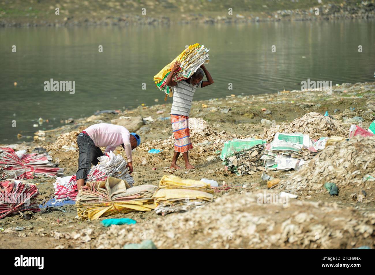 Des femmes risquent leur vie pour laver des sacs de ciment près de la rivière Surma à Sylhet. Il est nocif pour leur santé, et la poussière de plastique remplit aussi le lit de la rivière qui endommage l'environnement. L'exposition à des niveaux élevés de poussière de ciment irrite leur nez et leur gorge, ce qui pourrait entraîner de l'asthme professionnel et d'autres maladies. Le mortier peut également contenir de la silice cristalline respirable (RCS), qui se trouve également dans le béton et peut entraîner le développement de silicose ou de cicatrices des poumons, ce qui entraîne une perte de la fonction pulmonaire et un essoufflement sévère. Sylhet, Bangladesh. Banque D'Images
