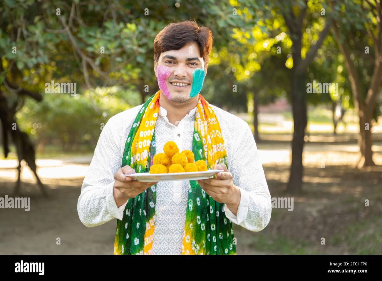 Jeune indien portant kurta blanc tenant une assiette de motichoor ladoos. Célébration du festival Holi dans le parc ou le jardin. Banque D'Images