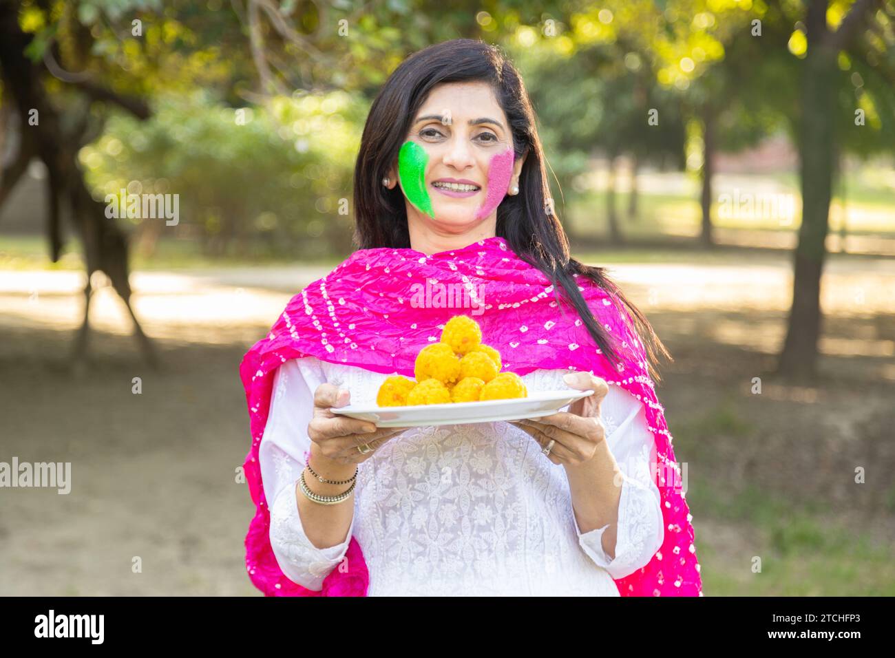 heureuse femme indienne portant kurta blanc tenant plaque de motichoor ladoos. Célébration du festival Holi dans le parc ou le jardin. Banque D'Images