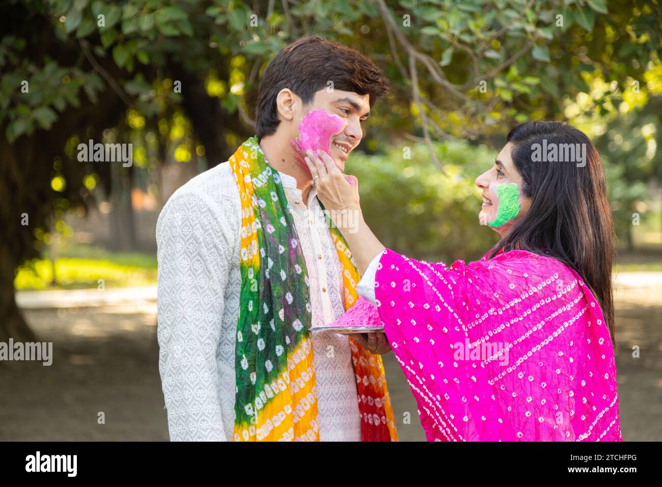 Heureux jeune couple indien portant kurta blanc jouant, mettant de la couleur sur le visage. Célébrer Holi ensemble en plein air dans le parc ou le jardin. Banque D'Images