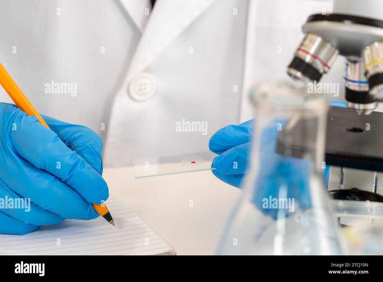 Gros plan de la main d'un scientifique portant des gants bleus et utilisant un microscope Banque D'Images