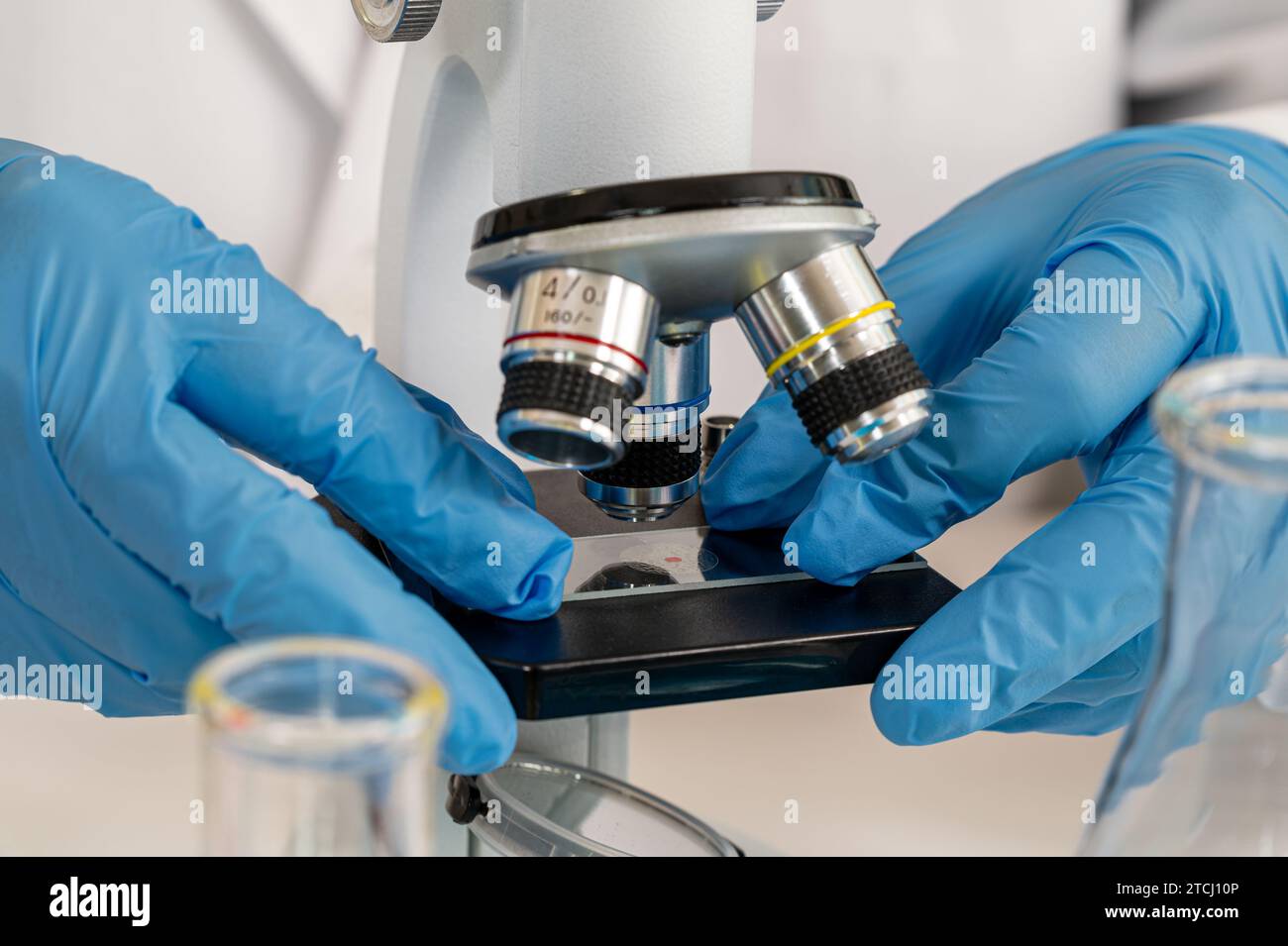 Gros plan de la main d'un scientifique portant des gants bleus et utilisant un microscope Banque D'Images