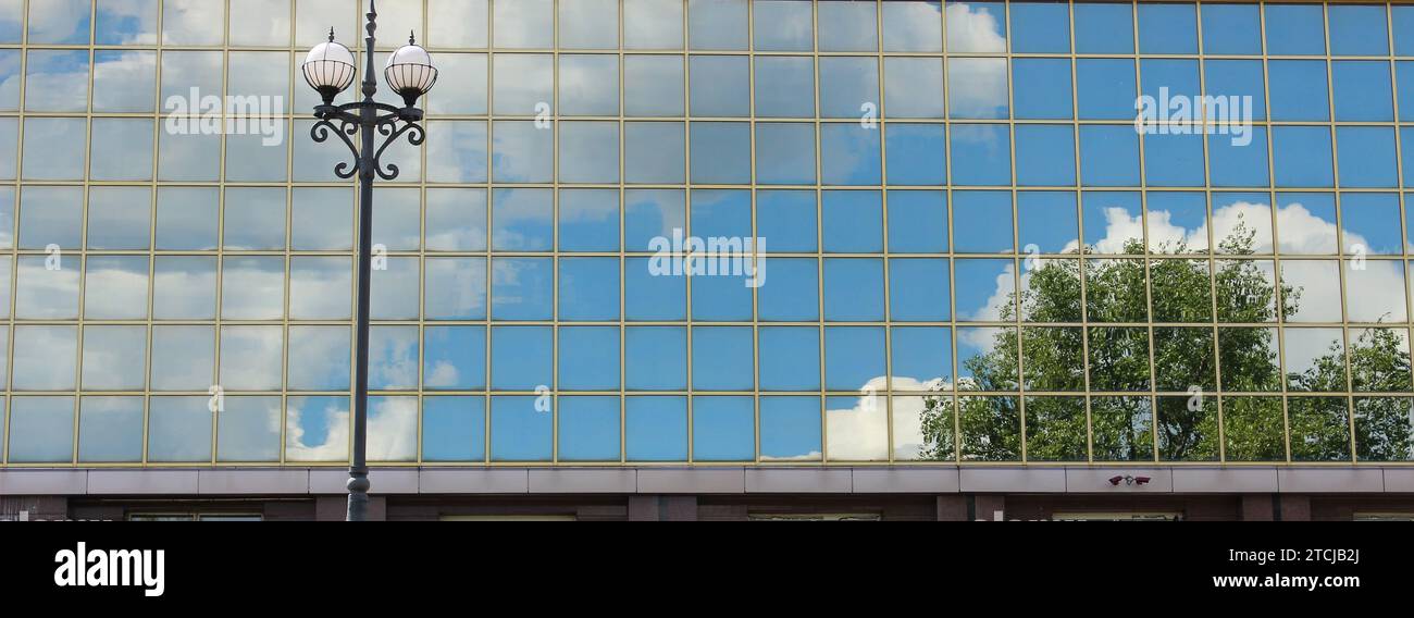 Reflet des arbres, du ciel et des nuages dans façade en verre du bâtiment moderne avec lampadaire en face Banque D'Images