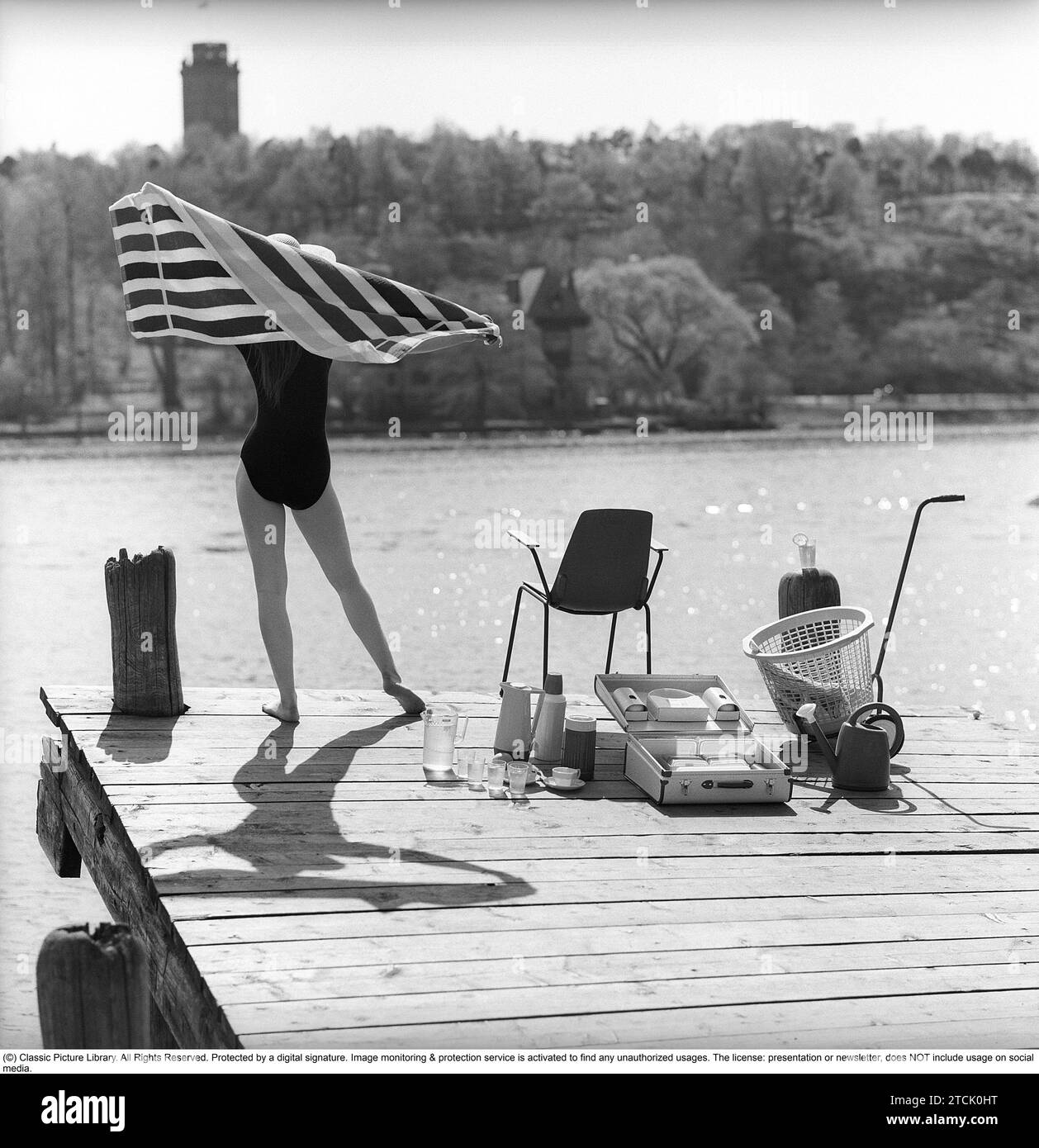 style de vie des années 1950. Une jeune femme au soleil portant un maillot de bain. Dans l'image, il y a beaucoup d'objets opportuns en plastique qui étaient populaires à l'époque. Surtout lorsque vous êtes en vacances d'été ou en camping. Un cas pratique pour les transporter. 1958 Kristoffersson réf DB96-1 Banque D'Images