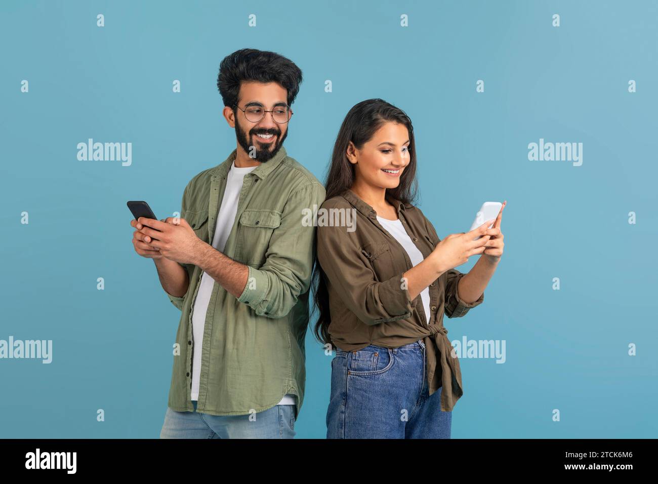 Sourire jeune homme indien avec smartphone espionner sa petite amie Banque D'Images