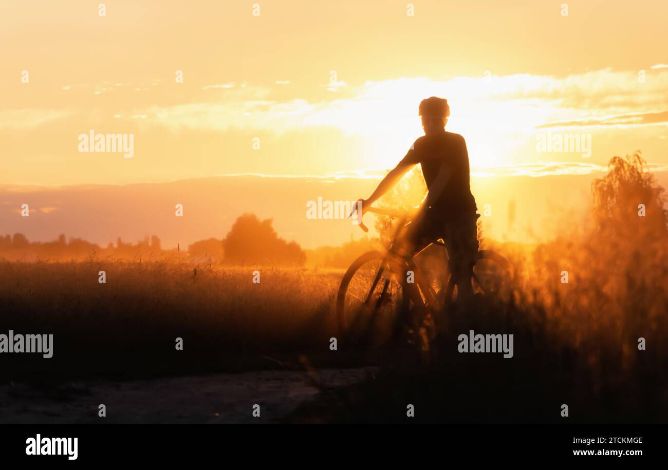 Silhouette de cycliste sur un chemin de terre de campagne au coucher du soleil. Flou sélectif. Banque D'Images