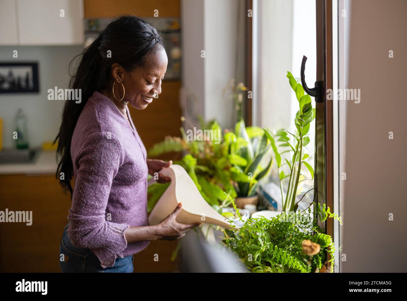 Belle femme arrosant les plantes à la maison Banque D'Images