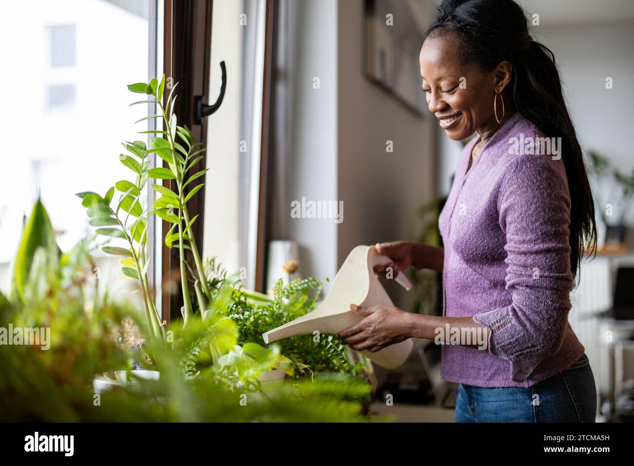 Belle femme arrosant les plantes à la maison Banque D'Images