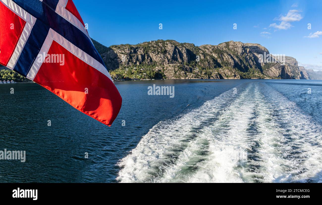 Bandera noruega en un barco ondeando al viento y el paisaje del Fiordo de la Luz o Lysefjord con la estela del barco, Stavanger, Noruega Banque D'Images
