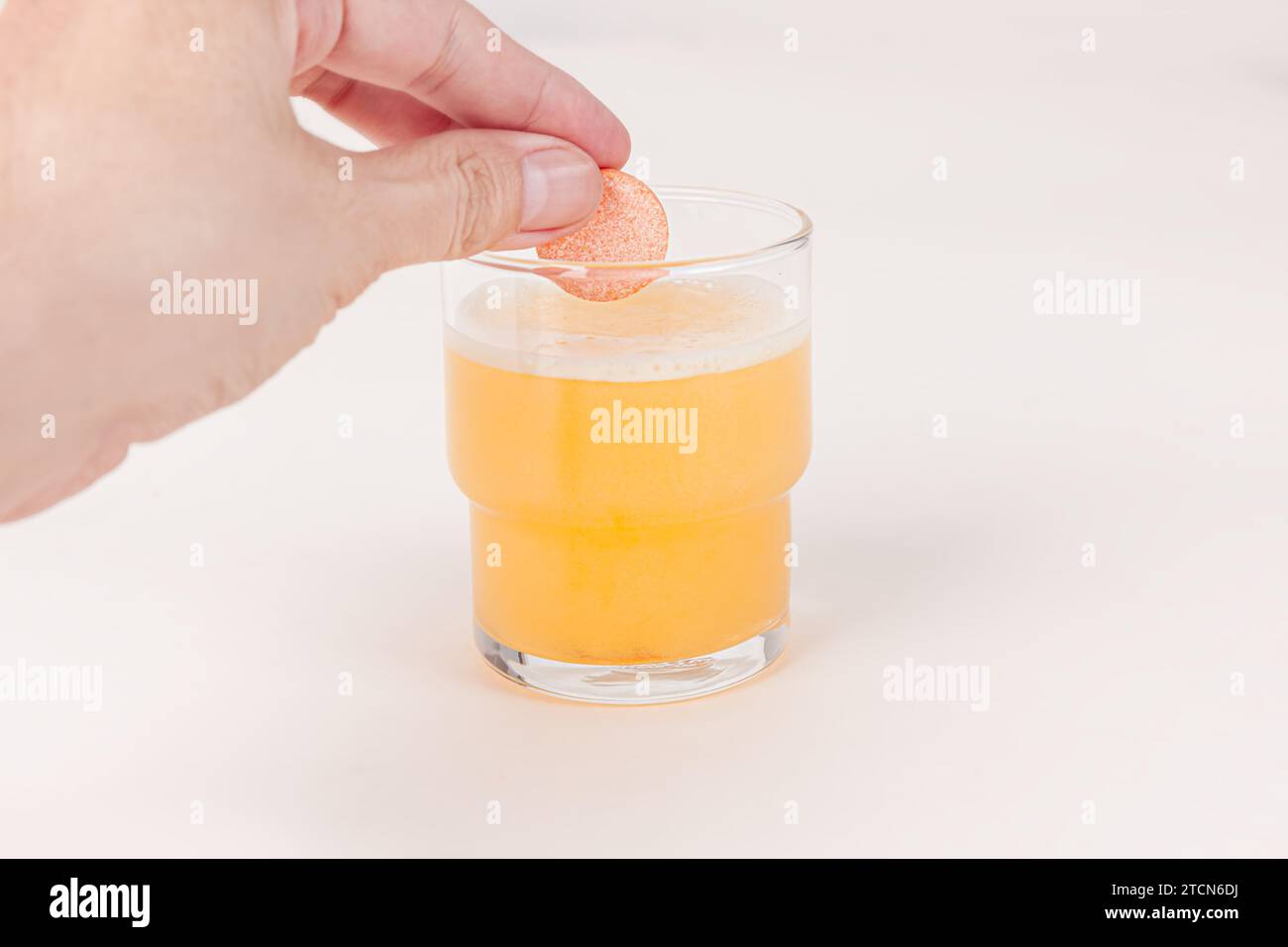 Main laissant tomber le comprimé effervescent orange de vitamine C dans un verre d'eau avec des bulles isolées sur fond blanc Banque D'Images