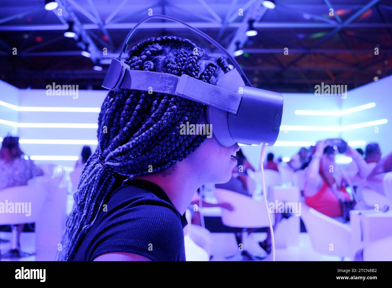 Fille de profil avec des tresses portant des lunettes de réalité virtuelle VR avec fond de lumières de néon verticalement Banque D'Images
