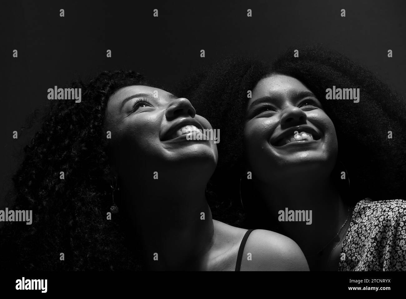 Portrait en noir et blanc de deux jeunes et beaux amis assis, regardant vers le haut souriant. Studio faible luminosité. Solide concept d'amitié. Banque D'Images