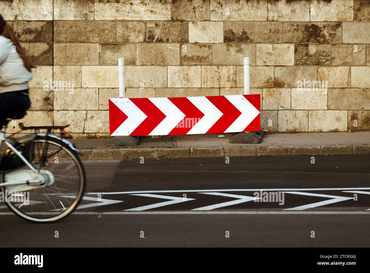 Panneau de direction contre le mur de pierre, fragment de cycliste passant Banque D'Images