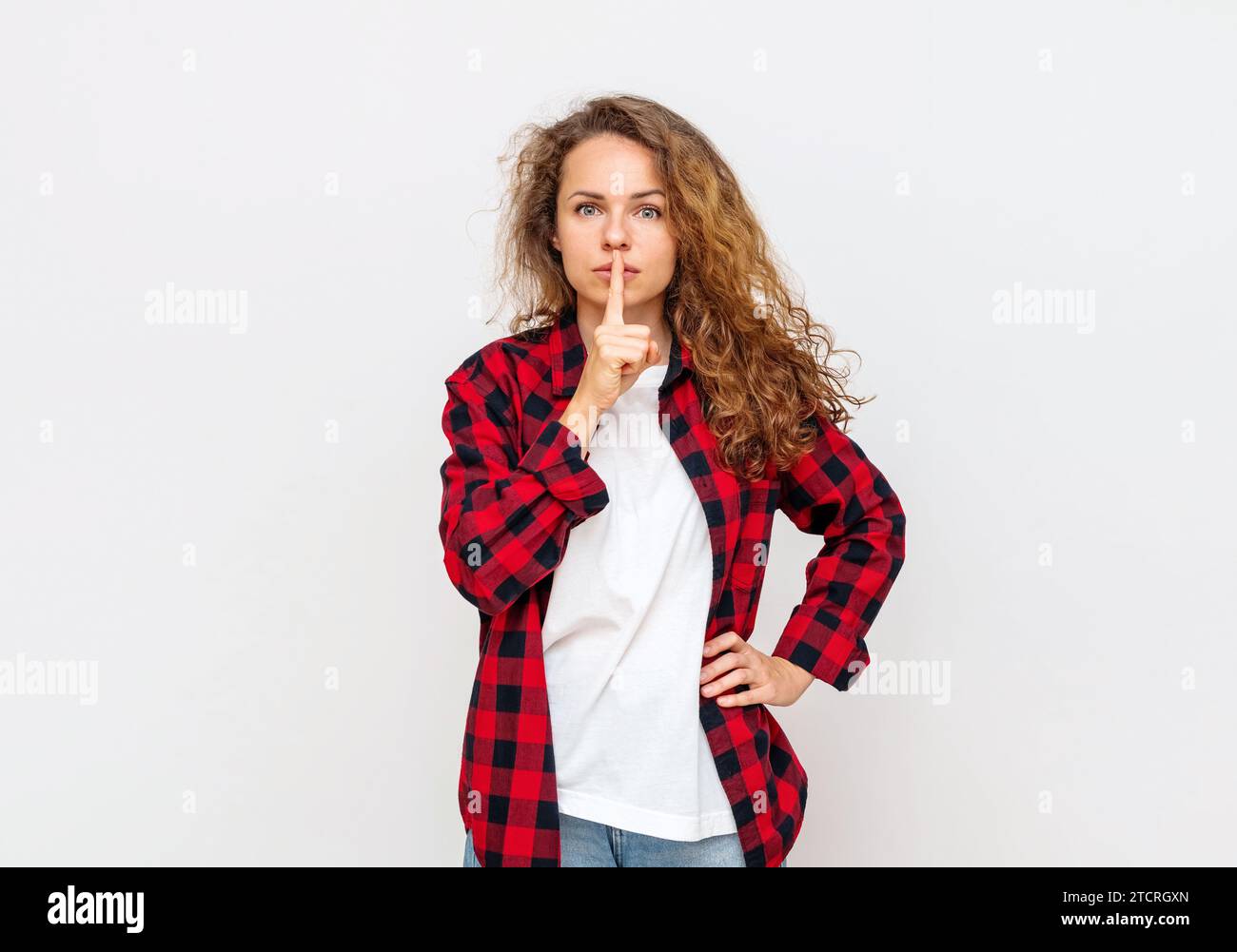 Femme aux cheveux bouclés shushing devant le fond blanc. Banque D'Images