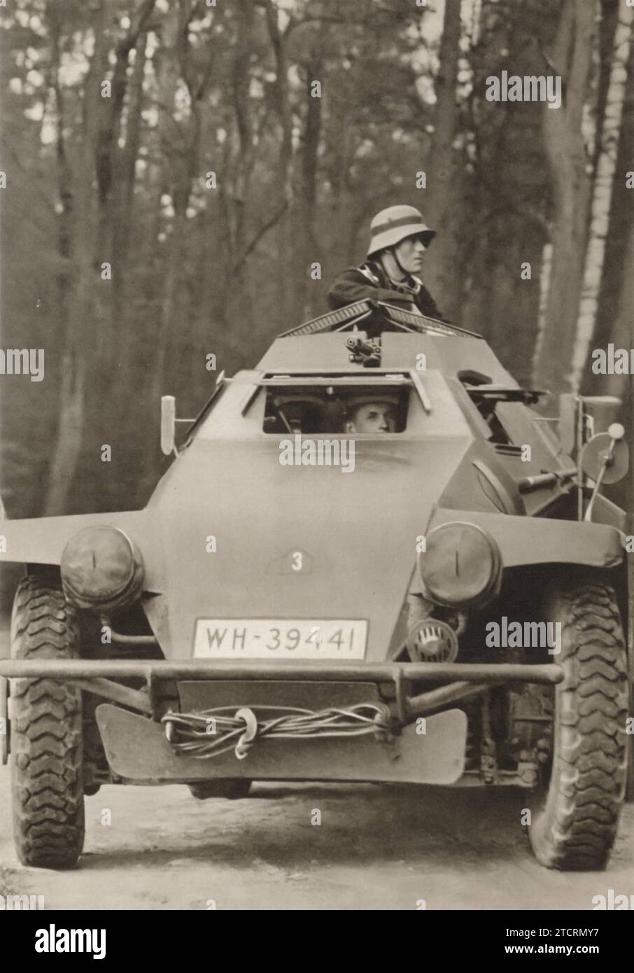 À l'intérieur d'un véhicule blindé compact, les soldats allemands assument leurs rôles : l'un en tant que conducteur, visible à travers la trappe avant, et l'autre en tant que mitrailleur principal, actionnant une mitrailleuse légère (LMG) depuis le haut du véhicule. Cette utilisation efficace de l'espace et de la répartition des tâches était caractéristique de la conception des véhicules blindés de l'armée allemande dans la période entourant la Seconde Guerre mondiale Banque D'Images