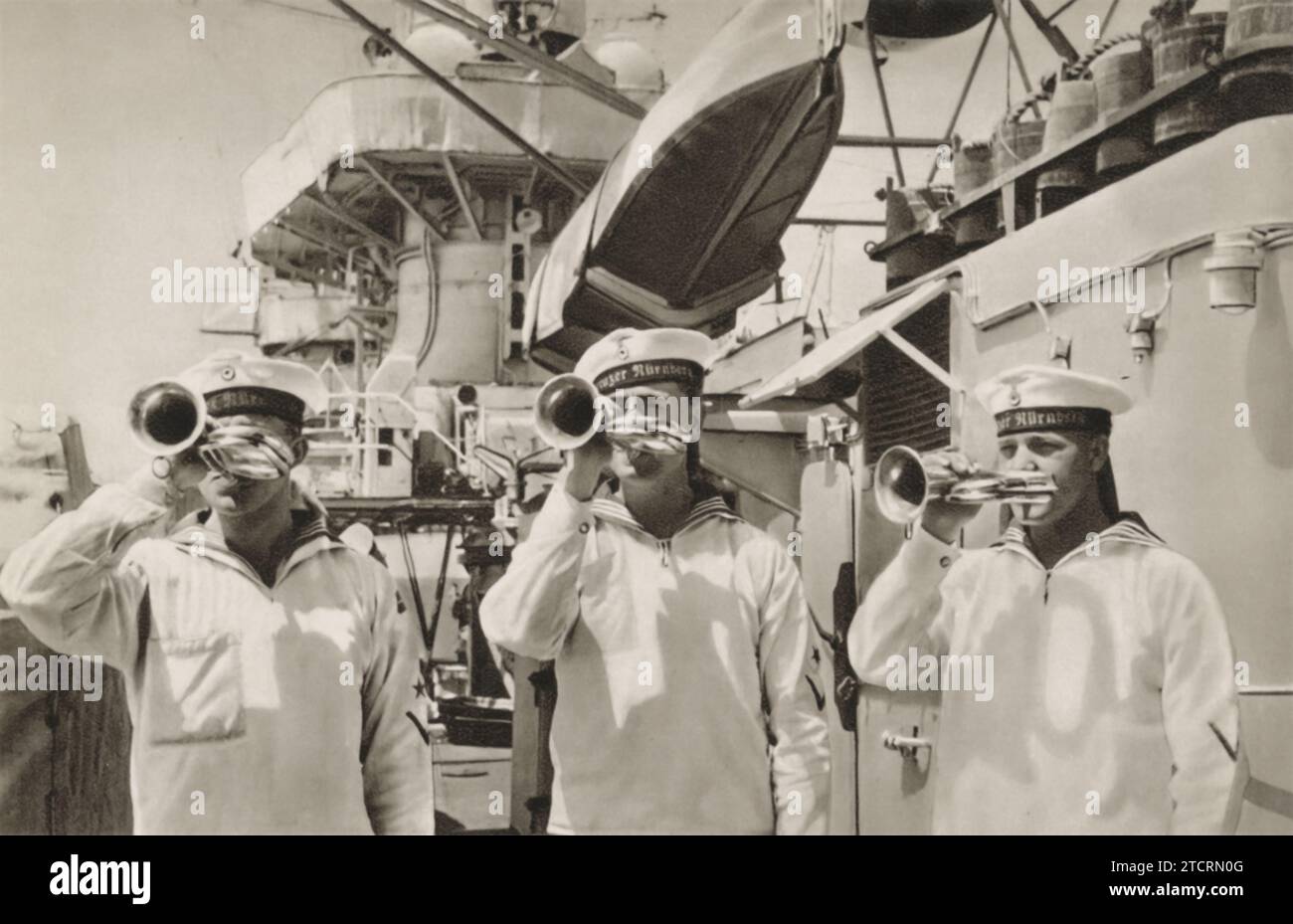 L'image montre les Marines allemands de la Kriegsmarine engagés dans un rituel de communication crucial à bord d'un navire : jouer de la trompette pour signaler le «rassemblement pour le service» à tous les soldats à bord. Cette pratique faisait partie intégrante de la vie sur les navires de la marine allemande pendant la Seconde Guerre mondiale, servant de repère auditif pour les marines de se rassembler pour le service ou les annonces importantes. Banque D'Images