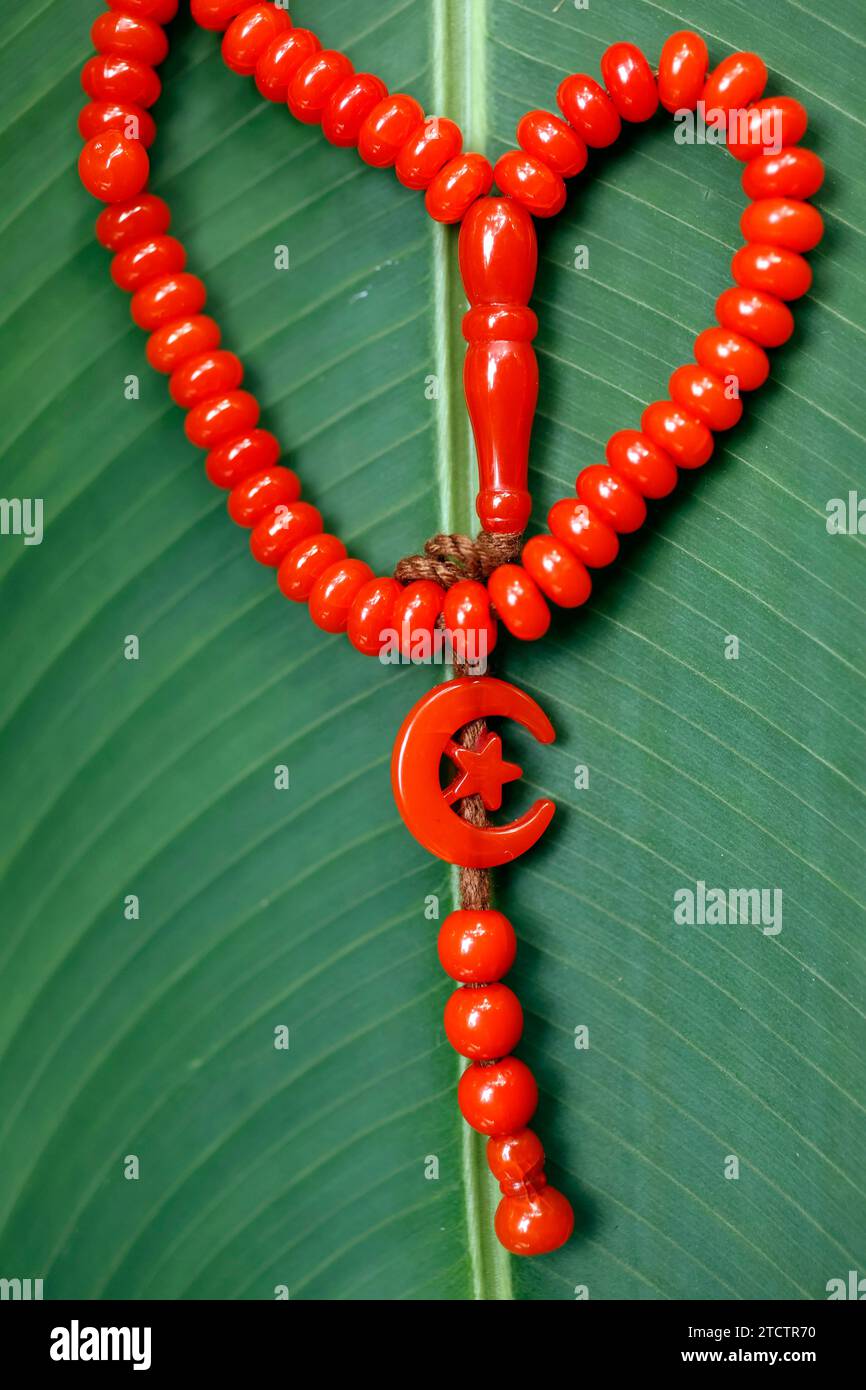 Tasbih rouge ( perles de prière musulmanes ) avec étoile et croissant sur une feuille verte. Banque D'Images