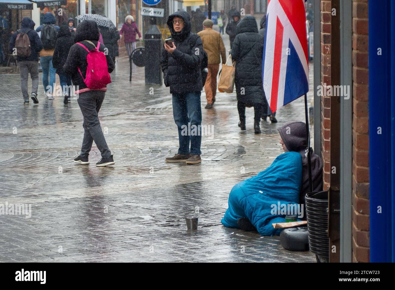 Windsor, Royaume-Uni. 14 décembre 2023. Reece, un homme qui a été rendu sans abri à la suite de la mort de son père, est assis sur le sol froid sous la pluie devant un magasin dans le riche Windsor, Berkshire, espérant que des passants lui donnent des pièces de monnaie. Polly Neate, directeur général de Shelter, a déclaré à Sky News que «le sans-abri n'est sur la liste de Noël de personne, mais 309 000 personnes passeront cette période de l'année dans une minuscule chambre d'auberge ou geler dans une porte». Crédit : Maureen McLean/Alamy Live News Banque D'Images Windsor, Royaume-Uni. 14 décembre 2023. Reece, un homme qui a été rendu sans abri à la suite de la mort de son père, est assis sur le sol froid sous la pluie devant un magasin dans le riche Windsor, Berkshire, espérant que des passants lui donnent des pièces de monnaie. Polly Neate, directeur général de Shelter, a déclaré à Sky News que «le sans-abri n'est sur la liste de Noël de personne, mais 309 000 personnes passeront cette période de l'année dans une minuscule chambre d'auberge ou geler dans une porte». Crédit : Maureen McLean/Alamy Live News Banque D'Images
