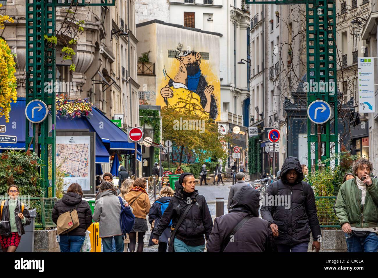 Les gens marchent le long de la rue Montorgueil, avec une peinture Street art de Tintin et le capitaine Haddock s'embrassant en arrière-plan sur un bâtiment à Paris, France Banque D'Images