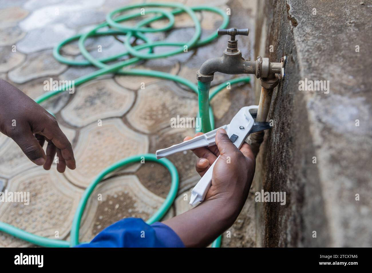 Gros plan des mains d'un plombier africain fixant le robinet extérieur. Banque D'Images