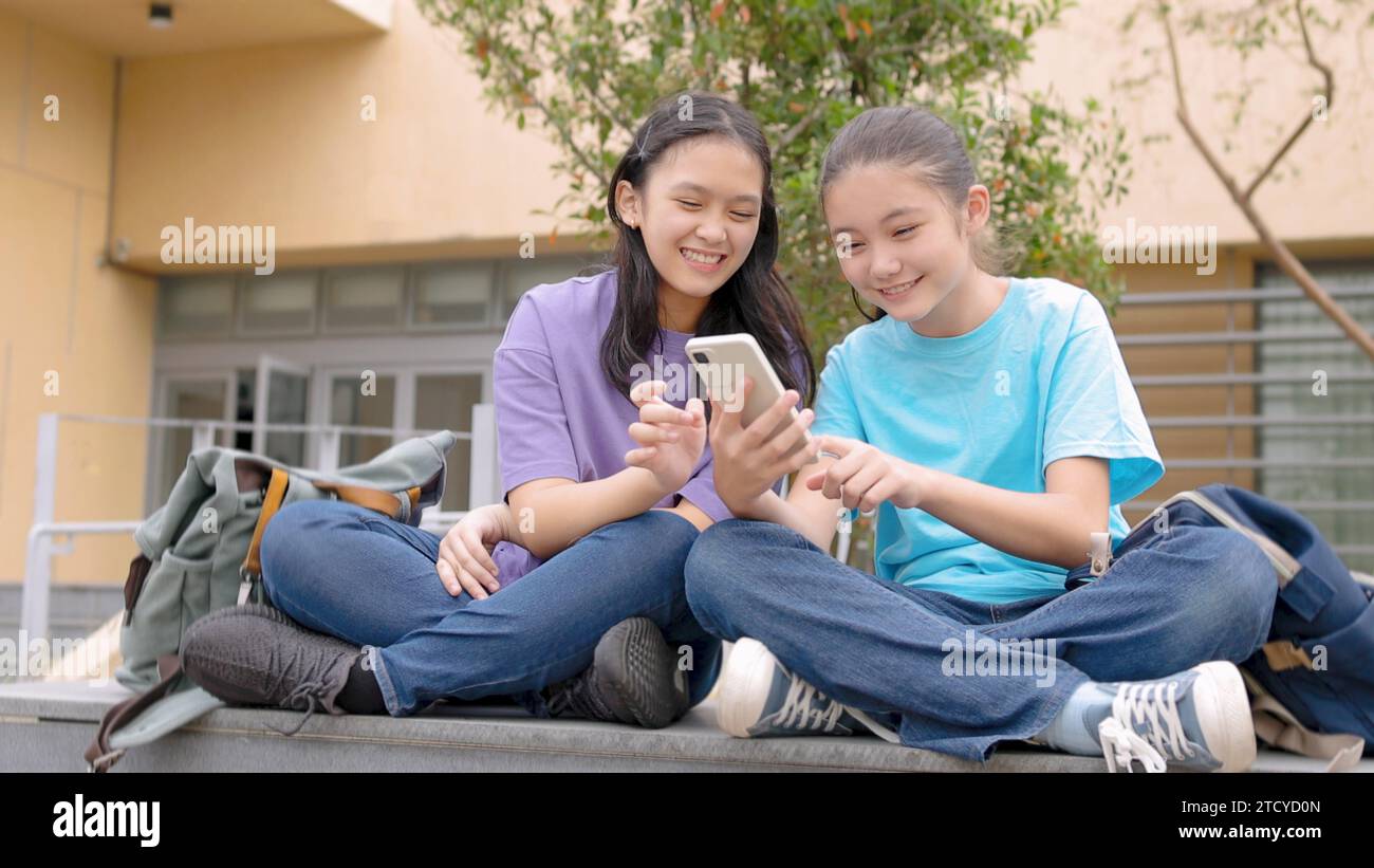 Filles étudiantes asiatiques heureuses utilisant un téléphone intelligent à l'école Banque D'Images