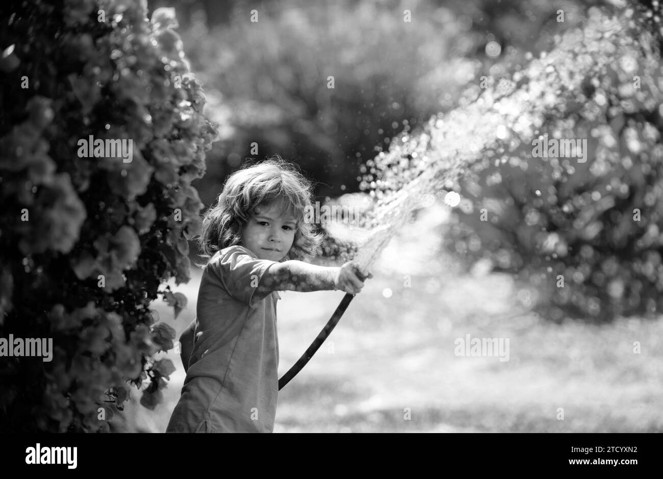 Arrosage des fleurs et des plantes par les enfants dans le jardin. Enfant avec tuyau d'eau dans l'arrière-cour. Jardinage pour enfants. Les enfants s'amusent à l'extérieur à la maison. Banque D'Images