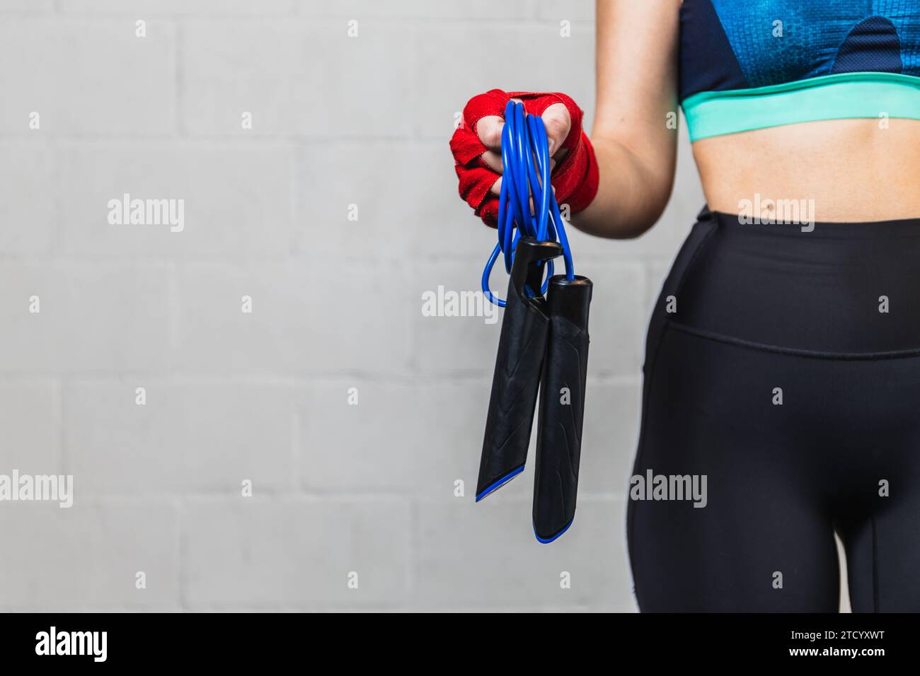 Photo horizontale fille horizontale caucasienne adolescente, habillée en vêtements de sport, avec des bandages rouges sur ses mains et une corde à sauter. Entraînement dans une salle de boxe. Banque D'Images