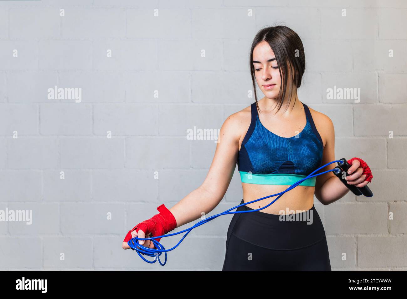 Photo horizontale adolescente caucasienne, vêtue de vêtements de sport, avec des bandages rouges sur les mains et une corde bleue. Entraînement dans une salle de boxe. Copier spa Banque D'Images