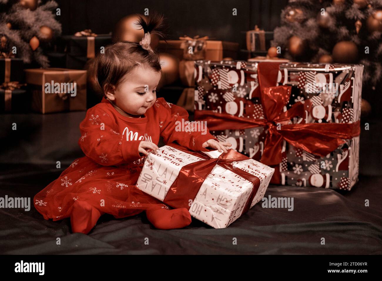 Une petite fille essayant d'ouvrir un cadeau de noël avec un arc Banque D'Images