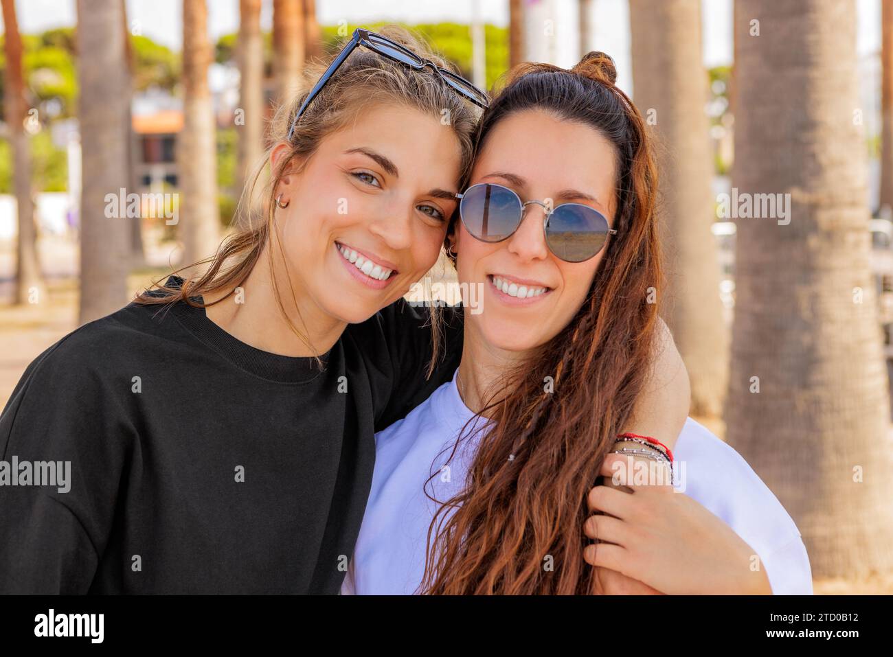 Portrait de jeune femme blonde caucasienne heureuse avec le bras autour d'un ami brunette portant des lunettes de soleil au parc pendant le week-end Banque D'Images