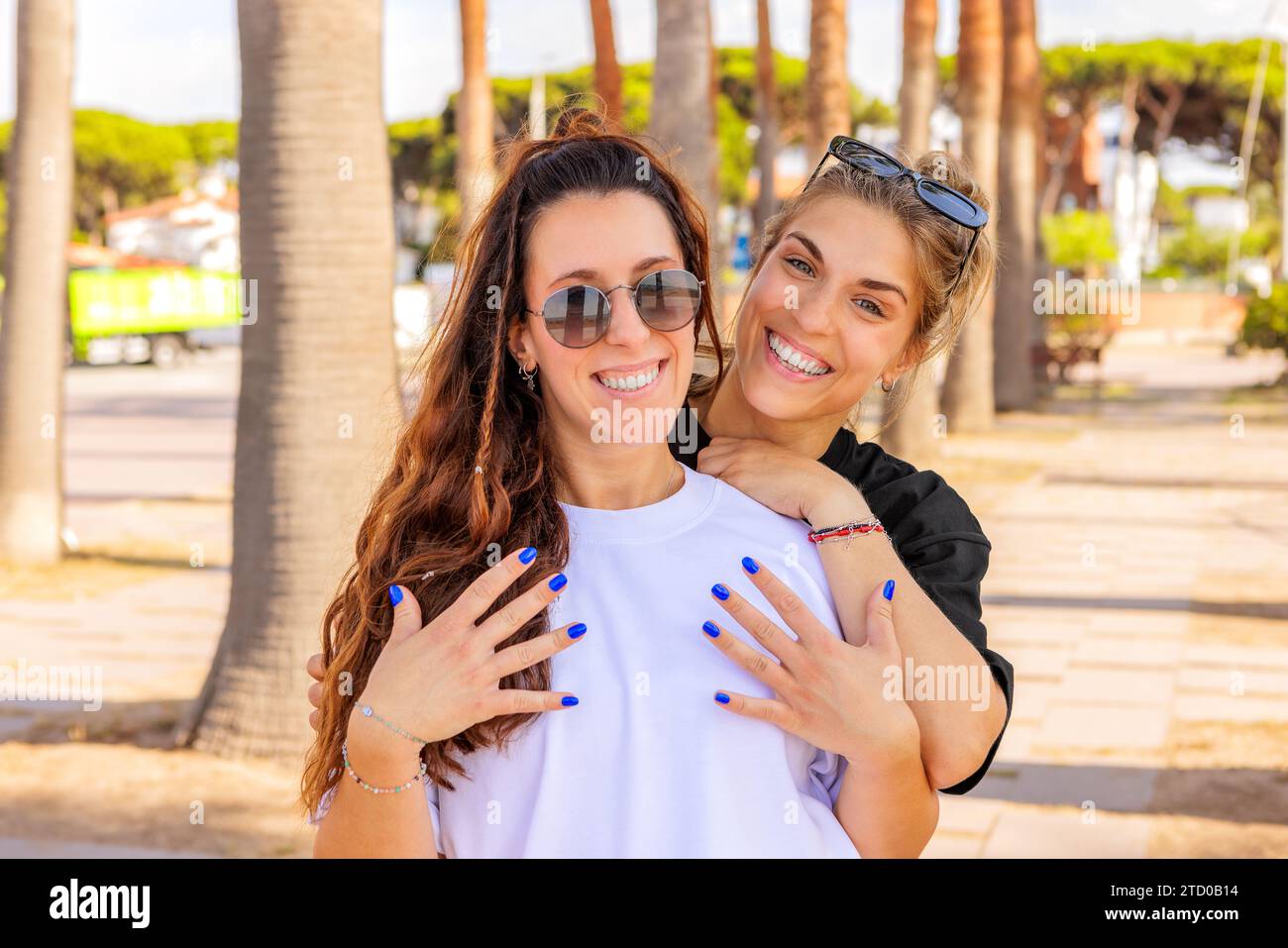 Portrait de jeune femme blonde caucasienne heureuse avec le bras autour d'un ami brunette portant des lunettes de soleil au parc pendant le week-end Banque D'Images