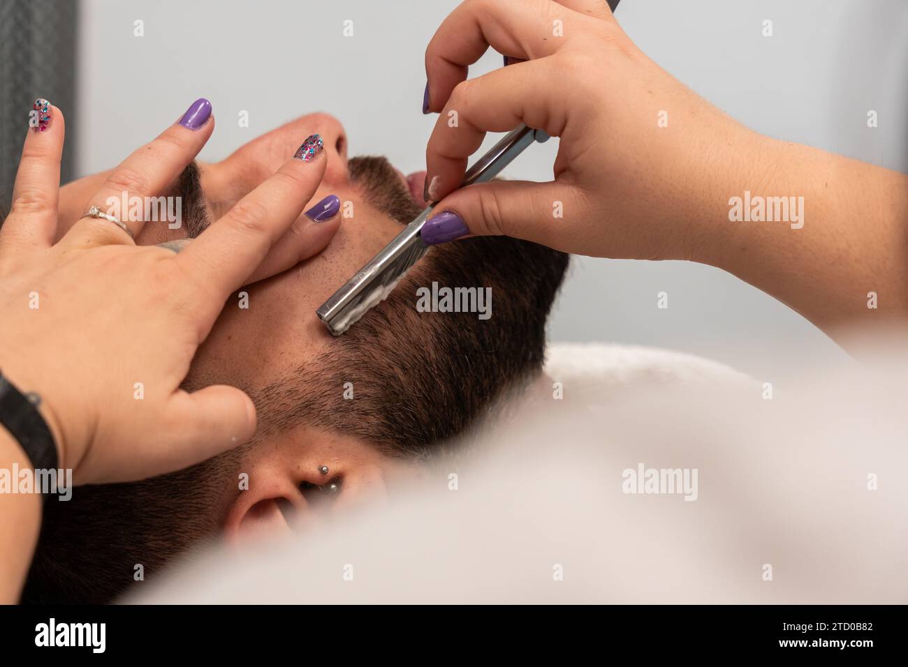 Vue latérale de la récolte mains méconnaissables de femme barbier rasant la barbe du client masculin avec rasoir droit au salon Banque D'Images