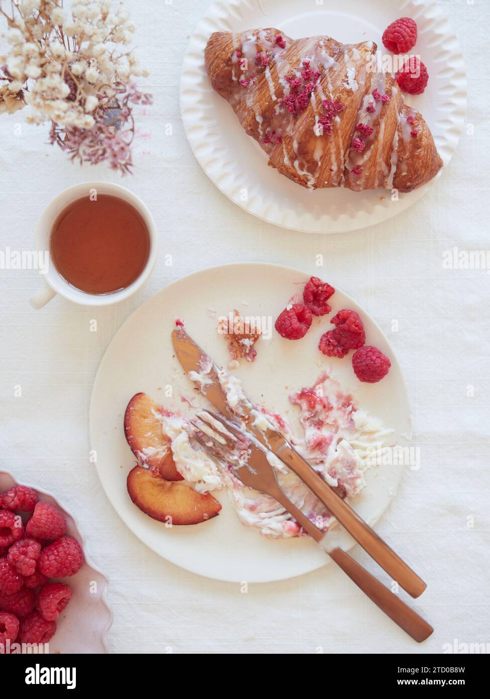 D'en haut de délicieux petit déjeuner avec croissant et thé servi sur des assiettes blanches avec framboise et couverts placés à table dans le restaurant Banque D'Images
