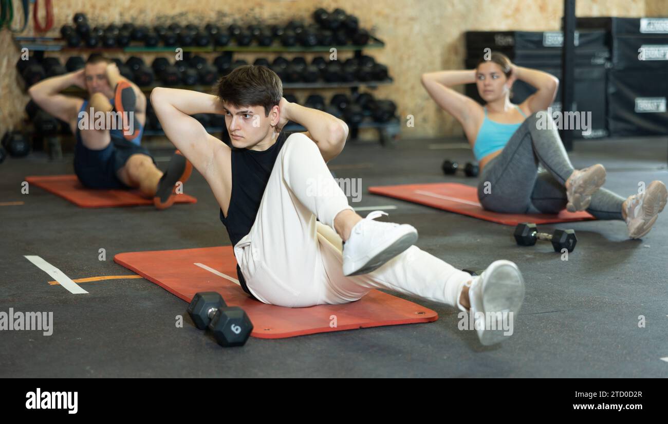 Homme athlétique faisant des exercices abdominaux pendant l'entraînement de groupe dans la salle de gym Banque D'Images