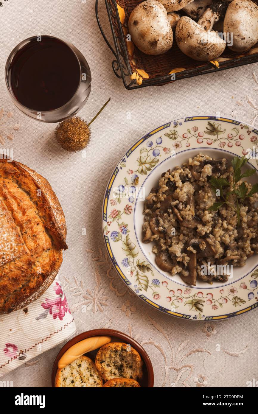 Vue aérienne d'une table rustique avec risotto aux champignons, pain frais et un verre de vin rouge. Banque D'Images