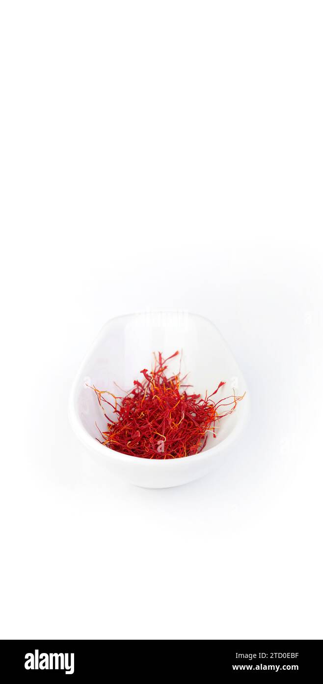 Gros plan d'un bol blanc rempli de fils de safran rouge vif, posé sur un fond blanc propre, soulignant la couleur riche et la texture de l'épice Banque D'Images