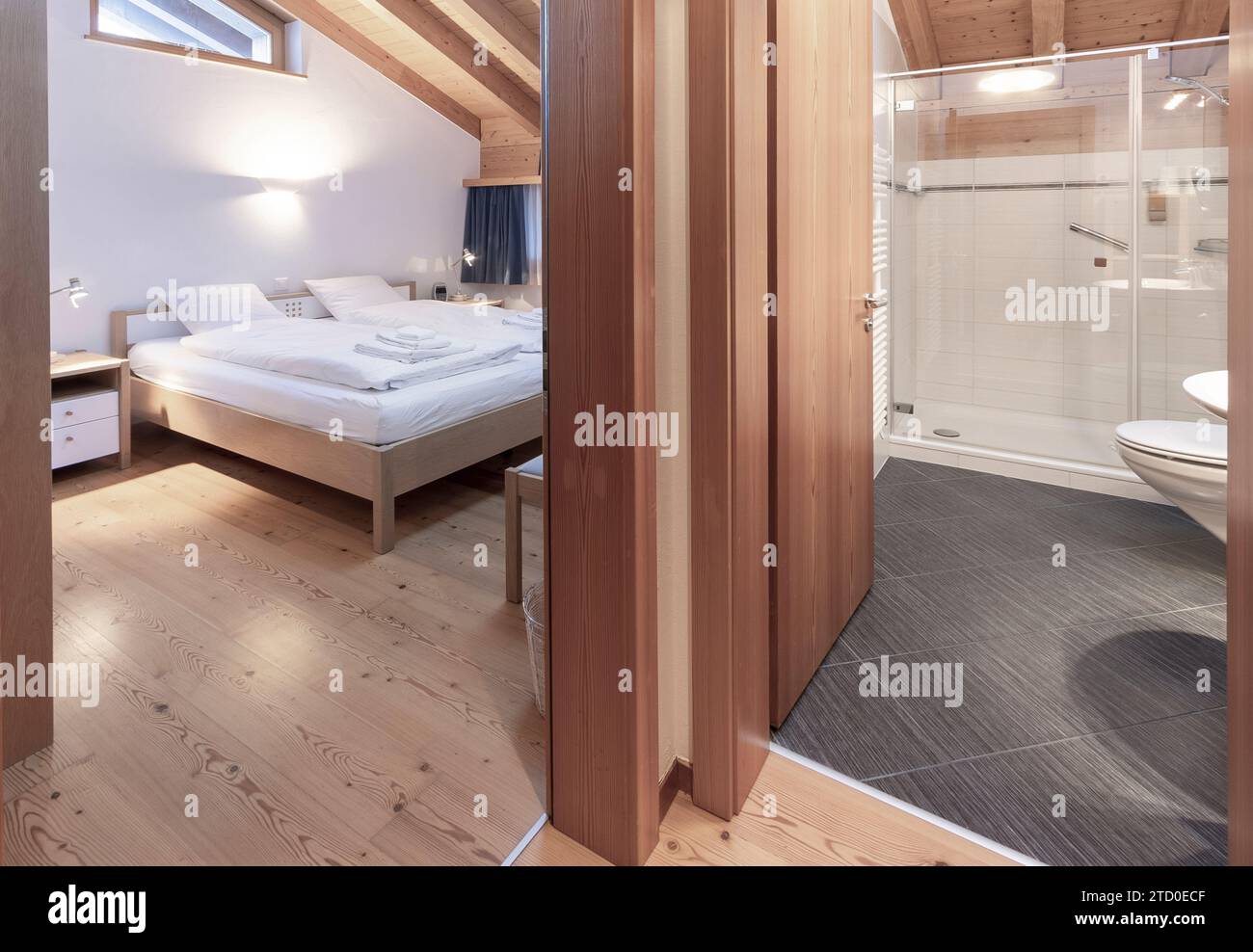 Une chambre et une salle de bain soigneusement entretenues avec un grand lit avec literie blanche et une salle de bain attenante, présentant un design épuré et contemporain avec woo Banque D'Images