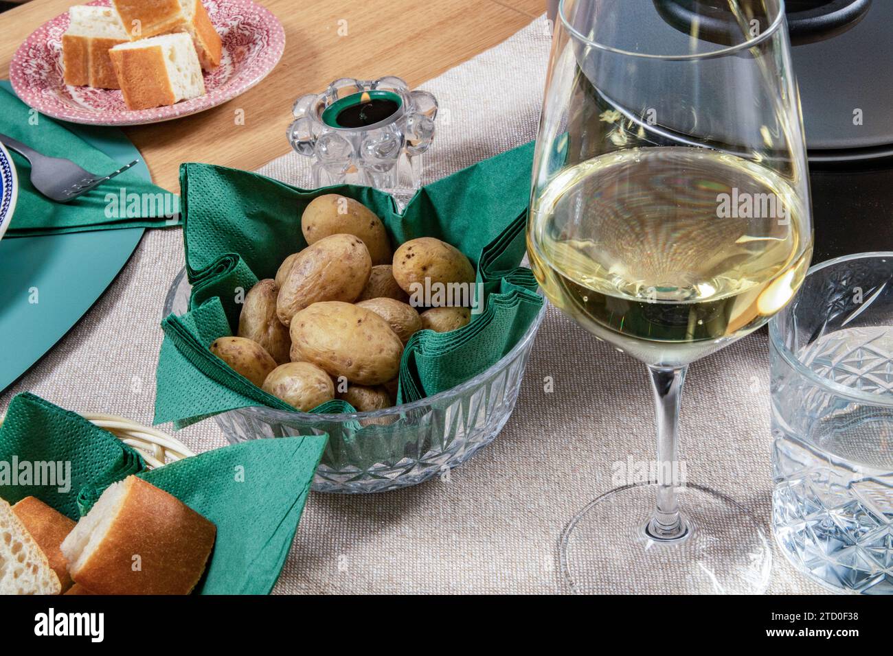 Une table sophistiquée avec un verre de vin blanc, du pain frais et un bol de pommes de terre cuites prêtes pour un dîner. Banque D'Images